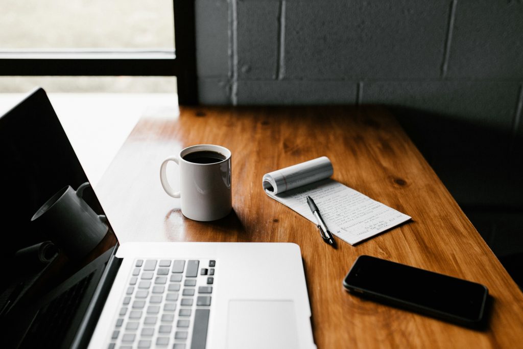 Side-on view of a wooden surface with a laptop, notepad, smartphone, and cup of coffee