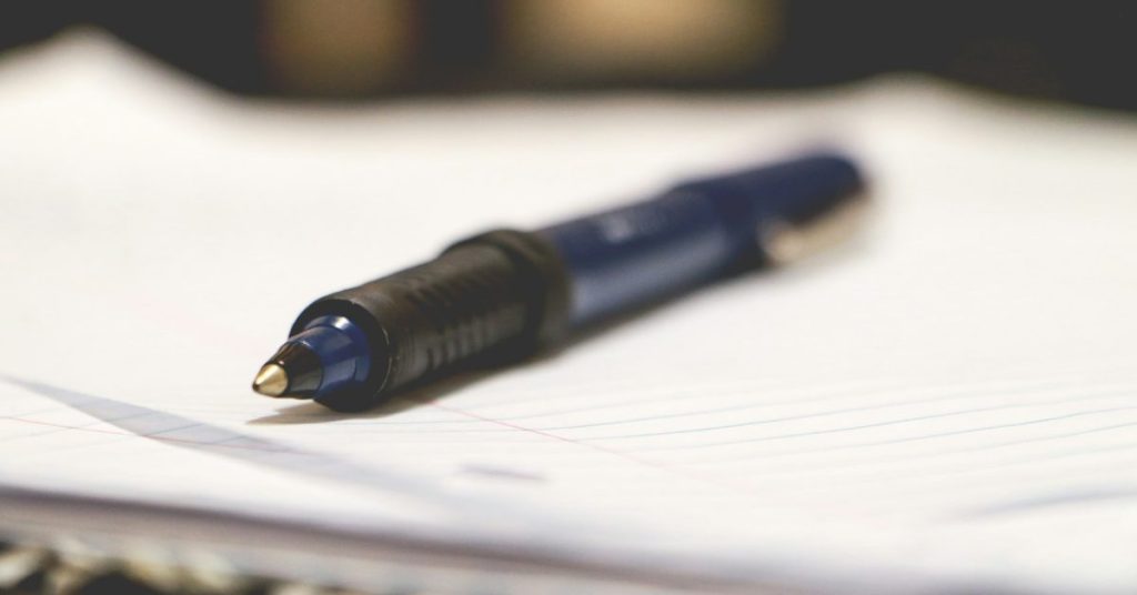 Close-up of a pen resting on blank paper, with the nib in sharp focus and the background softly blurred.