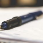 Close-up of a pen resting on blank paper, with the nib in sharp focus and the background softly blurred.
